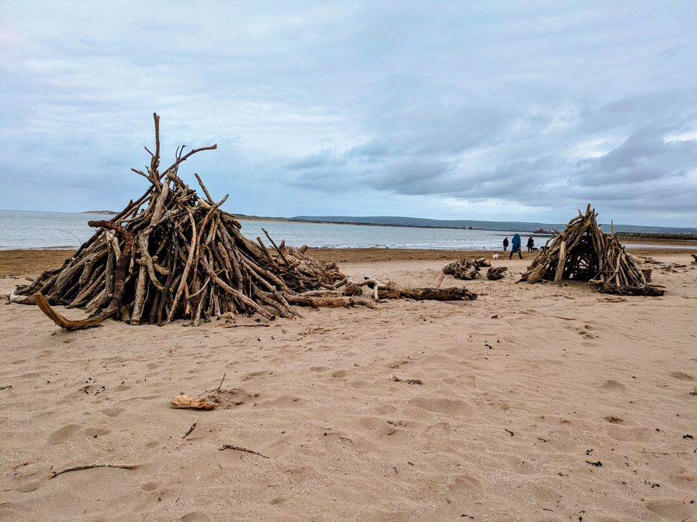 Driftwood structures on a beach with people walking near the ocean at Blackbird Cottage Northam
