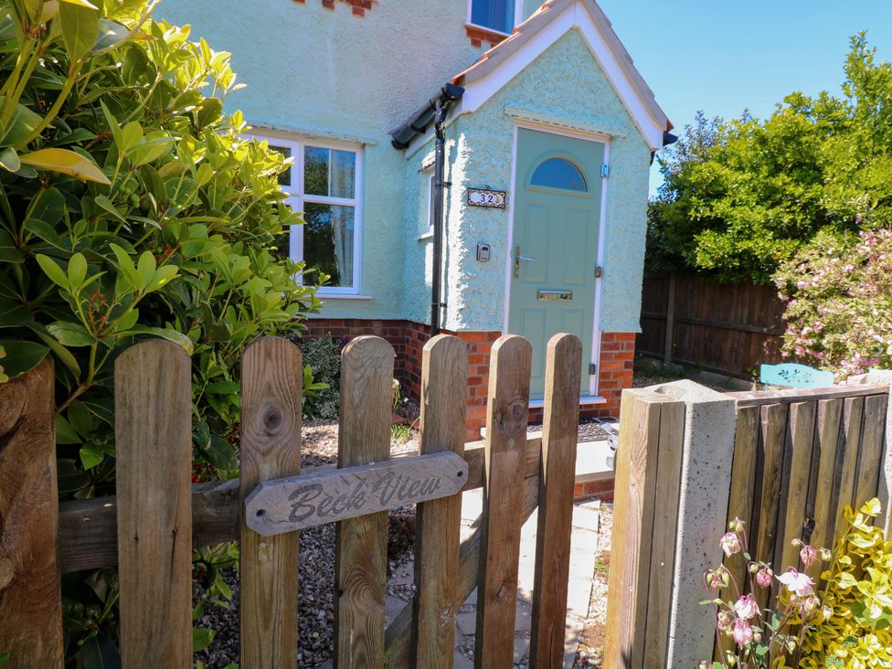 A wooden gate with a Beck View sign leading to a small house with a light blue door and green plants in Sheringham