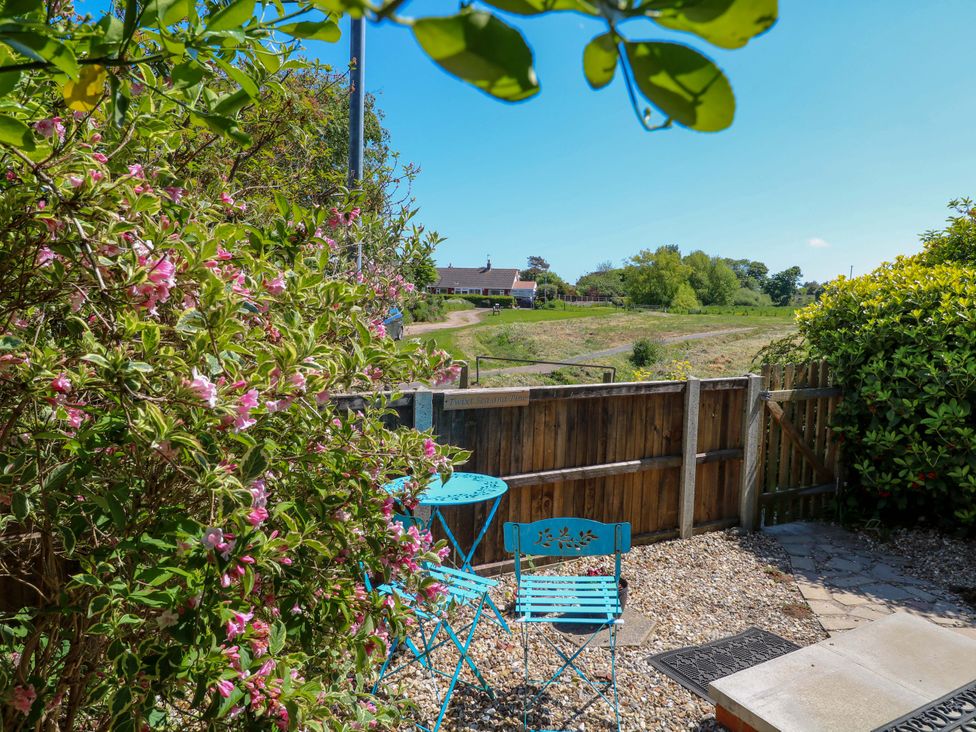 A garden patio with a blue metal table and two chairs next to a wooden fence and flowering plants at Beck View in Sheringham