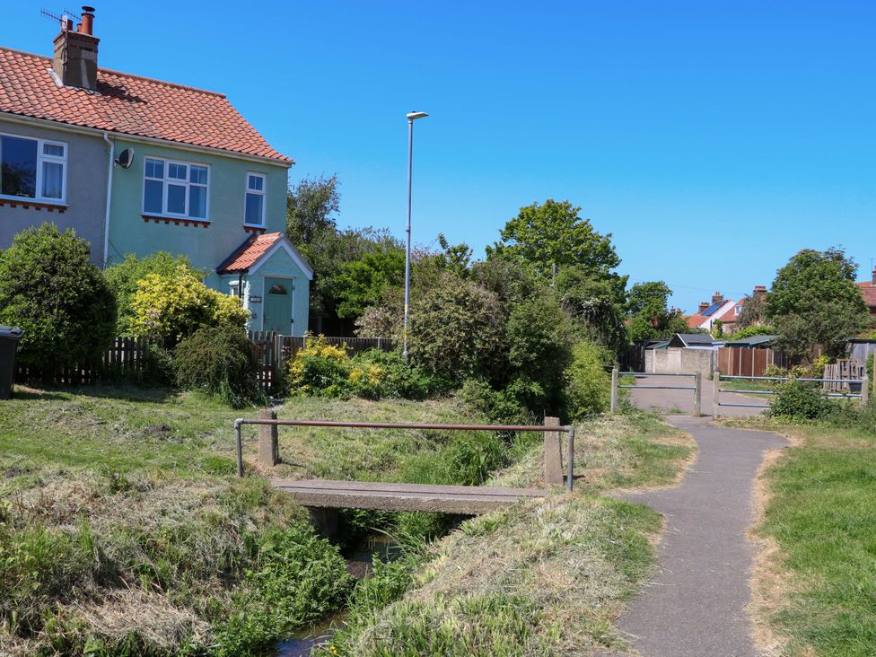 A small concrete footbridge over a narrow stream next to a pathway with houses and vegetation in the background at Beck View in Sheringham