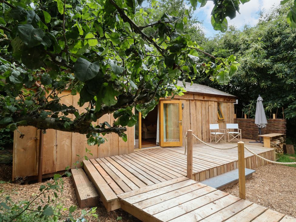 A wooden cabin with a deck and outdoor seating at Brambly Cabin in Crediton