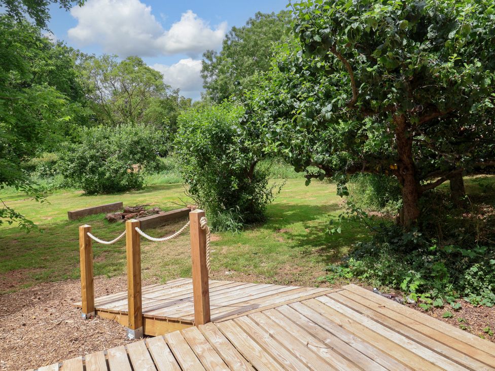 A garden with a wooden walkway and trees at Brambly Cabin in Crediton