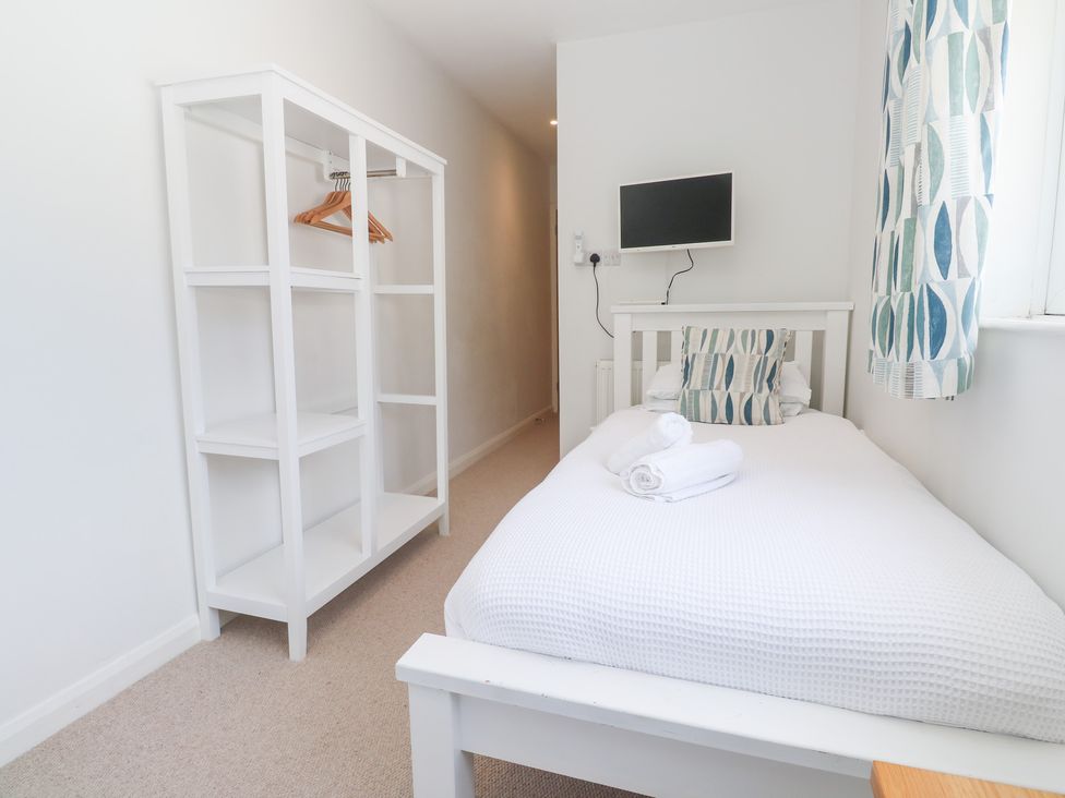 A bedroom with a bed, shelf, and television at Foundry Cottage In Hayle Harbour, Hayle