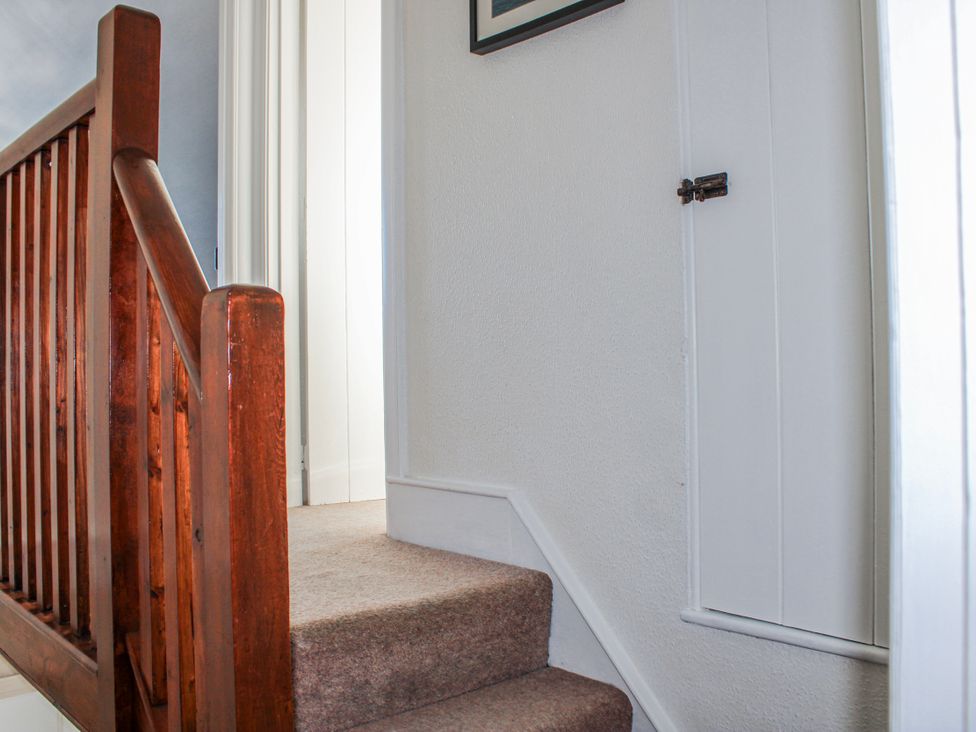 A staircase with a wooden handrail and a door at Waders in Salcombe