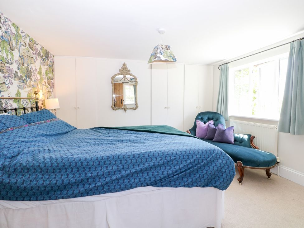 A bedroom with a bed and an armchair at Cherry Garden Cottage Sandhurst