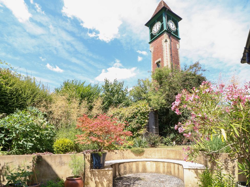 A garden with a clock tower and flowers at Cherry Garden Cottage in Sandhurst