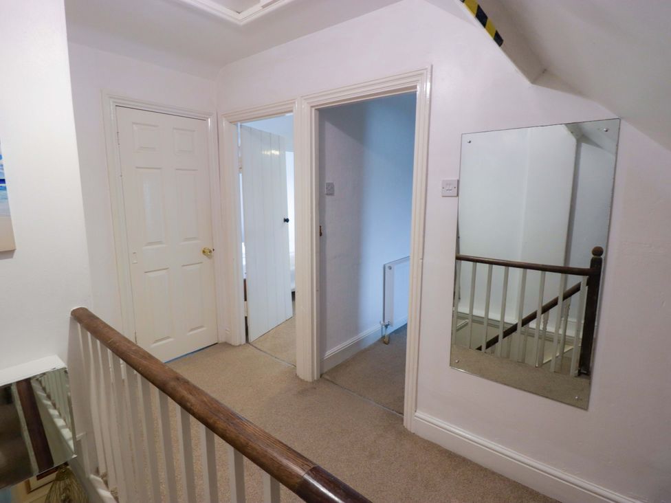 A hallway with a mirror and doors at Gwylan Maisonette in Tenby