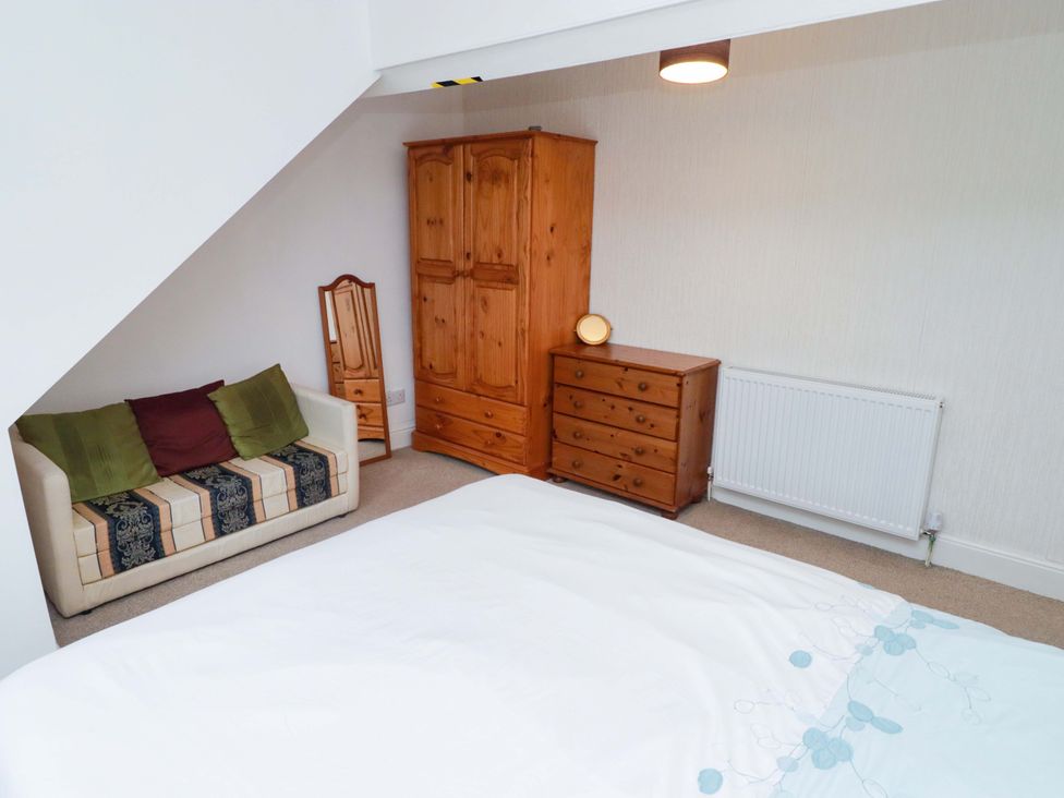 A bedroom with a bed, sofa, wardrobe, and chest of drawers at Gwylan Maisonette in Tenby