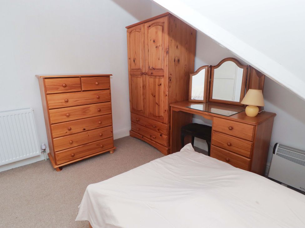 A bedroom with a bed, dresser, wardrobe, and mirror at Gwylan Maisonette in Tenby