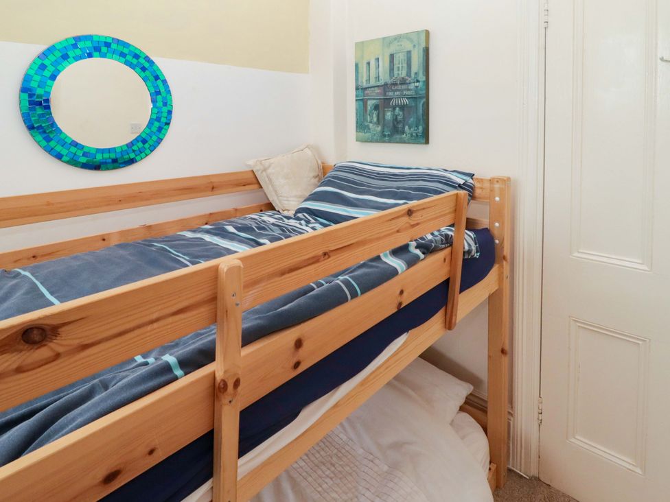 A bunk bed with striped bedding and a mirror at Gwylan Maisonette in Tenby