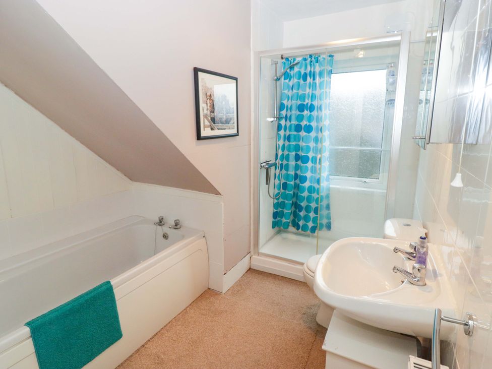 A bathroom featuring a bathtub, shower, and sink at Gwylan Maisonette in Tenby