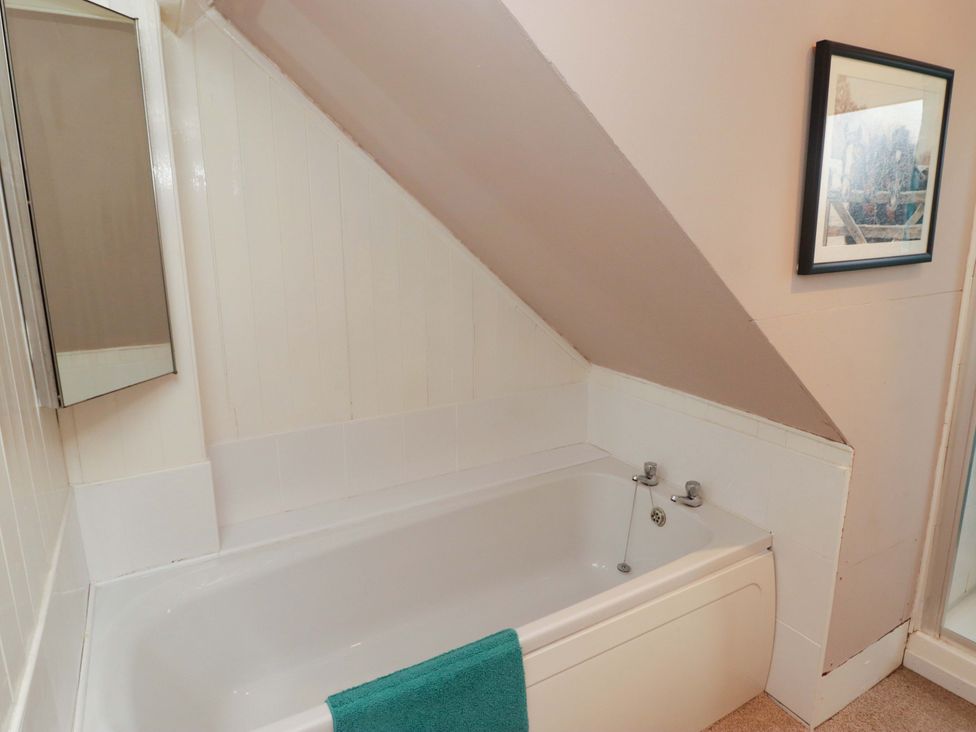A bathroom with a bathtub and a mirror at Gwylan Maisonette Tenby