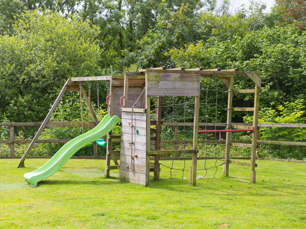 A play structure with a slide and swing in an outdoor play area at Branock, Tor Down Quarry in St Breward