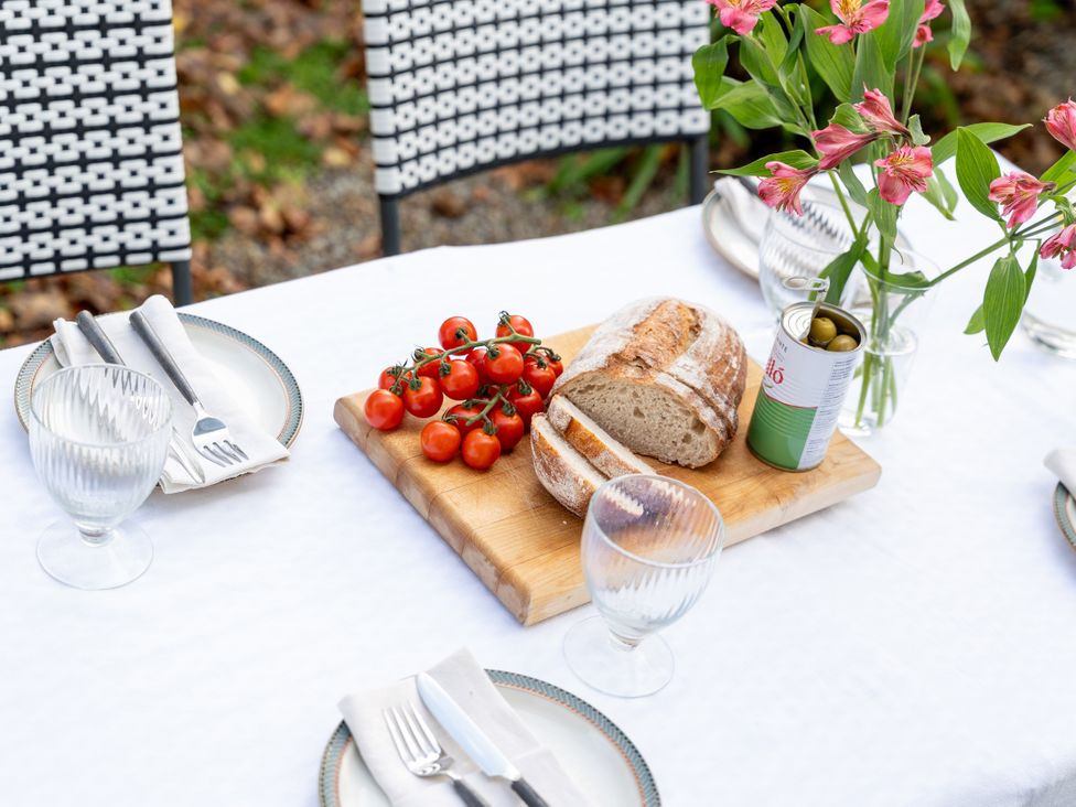 An outdoor dining table with bread, tomatoes, and a flower arrangement at Estuary Watch Lelant near Carbis Bay