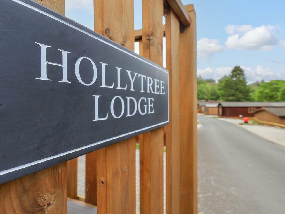 A wooden fence with a Hollytree Lodge sign and a road with wooden buildings in the background at Hollytree Lodge Beckside 1 Limefitt Park near Windermere