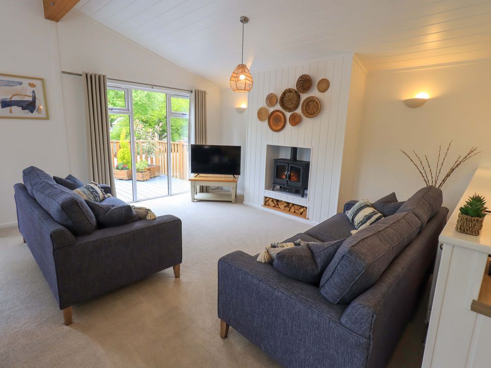 A living room with two blue sofas a wood burning stove and a television at Hollytree Lodge Beckside 1 Limefitt Park near Windermere