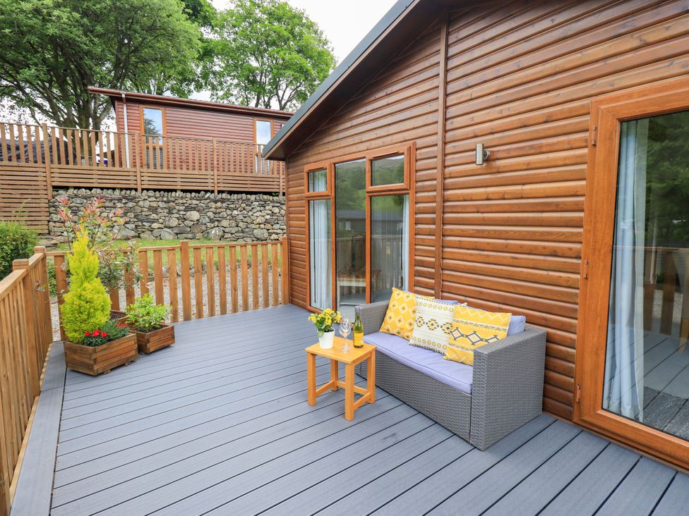 An outdoor deck with a small sofa and a table with a bottle and glasses at Hollytree Lodge Beckside 1 Limefitt Park near Windermere