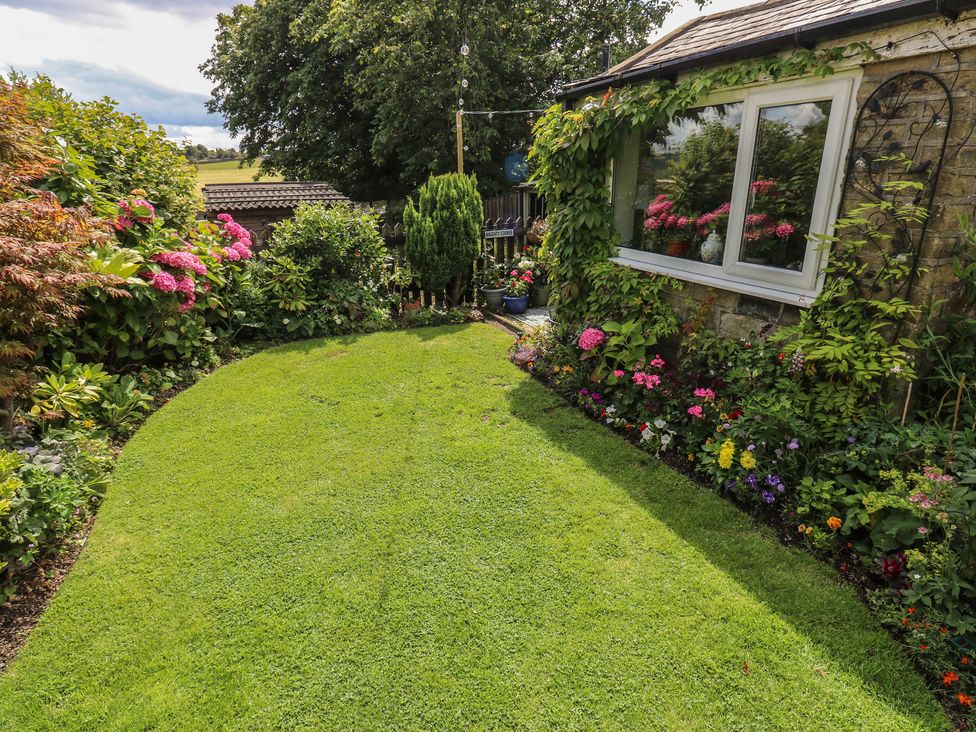 A garden with grass and flower beds at Prospect Cottage in Ripponden