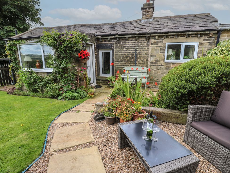 A garden area with a cottage, a glass table, and potted plants at Prospect Cottage in Ripponden