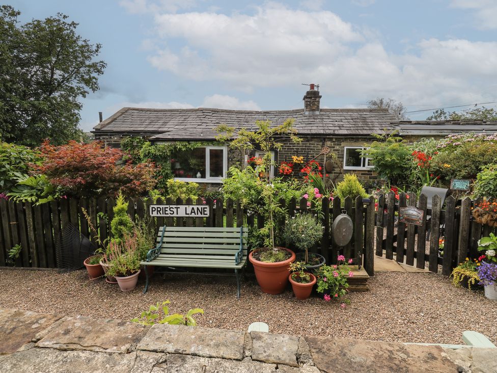 A garden with a bench and flower pots at Prospect Cottage in Ripponden