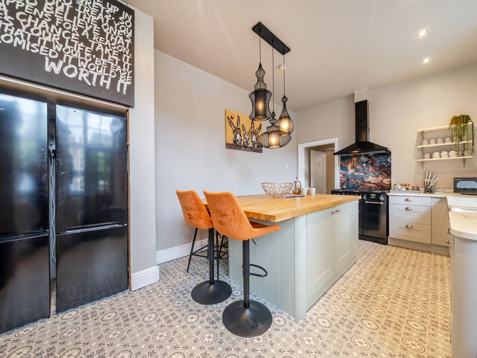 A kitchen with a refrigerator, bar stools, and a kitchen island at The Keep in Llandudno