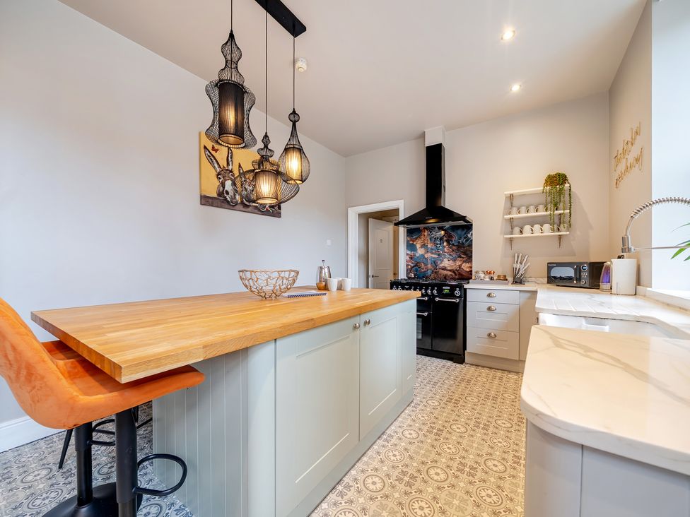 A kitchen with an island, bar stools, and appliances at The Keep in Llandudno