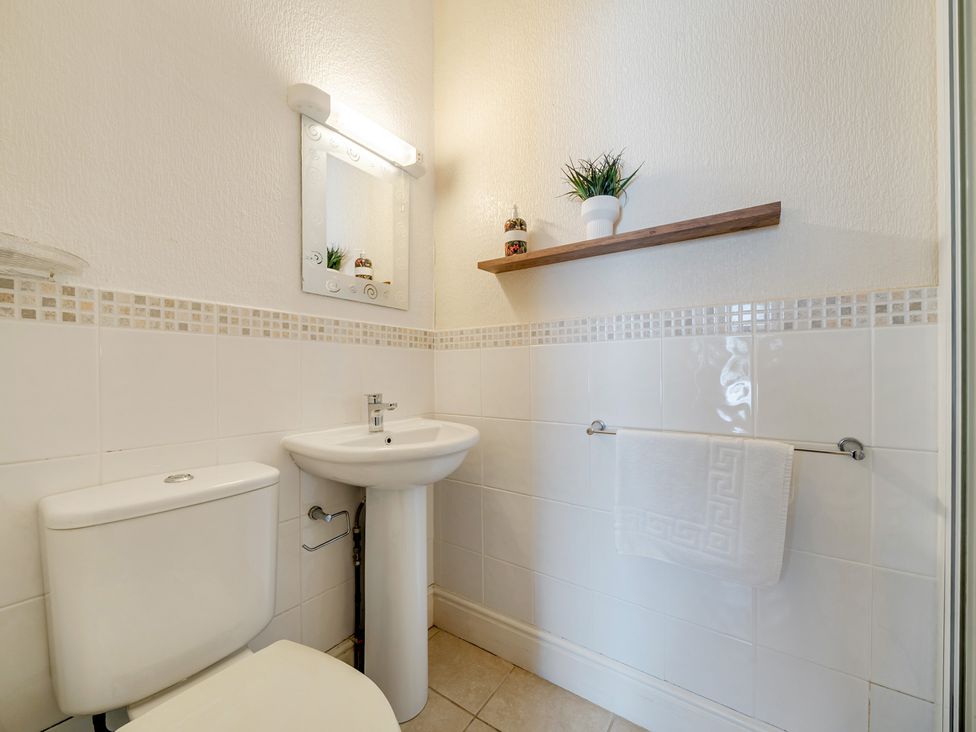 A bathroom with a toilet, sink, and shelf at The Keep in Llandudno