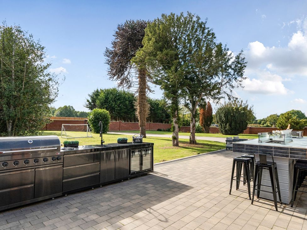 An outdoor kitchen with grill and bar stools at Otherton Hall Penkridge