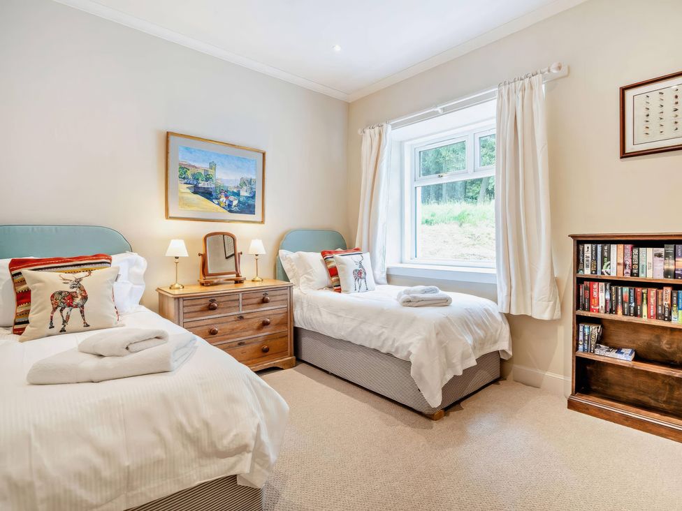 A bedroom with two beds and a bookshelf at Upper Hillside Cottage Blairgowrie