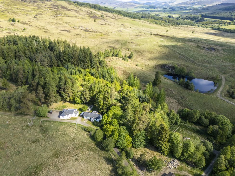An aerial view of a house surrounded by trees and a pond at Upper Hillside Cottage in Blairgowrie