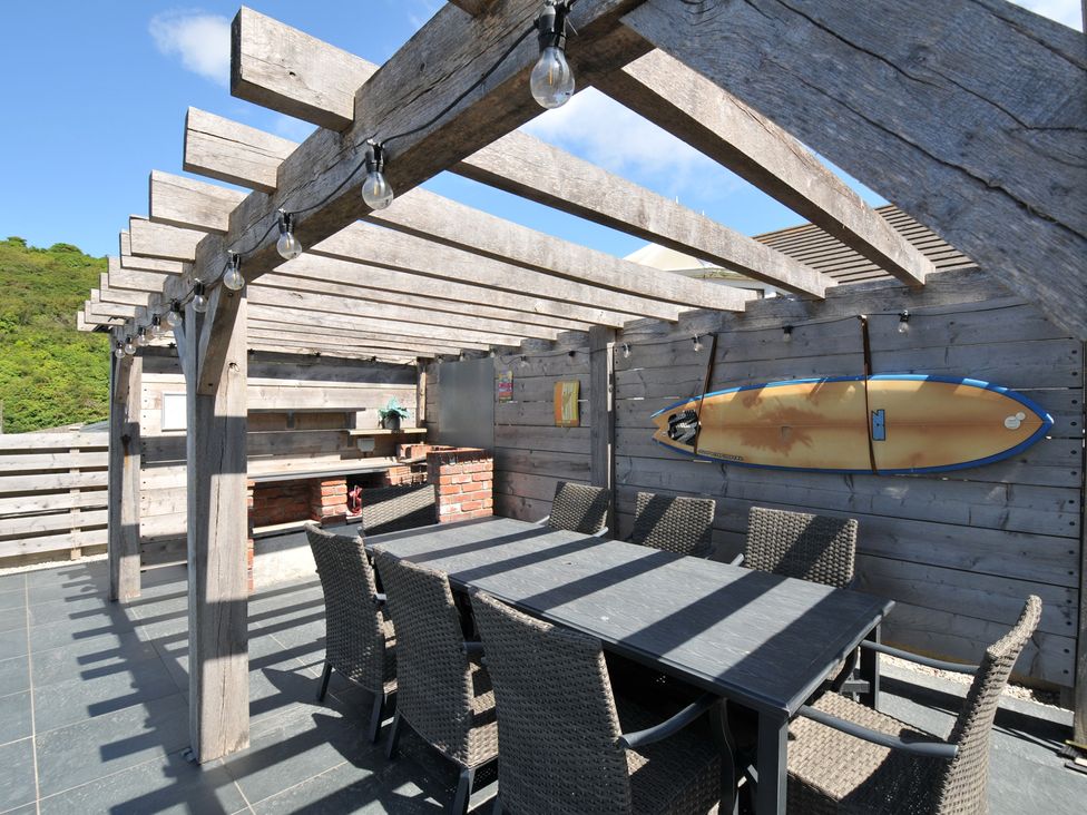An outdoor dining area with a table and chairs under a pergola at Breakers View in Polzeath