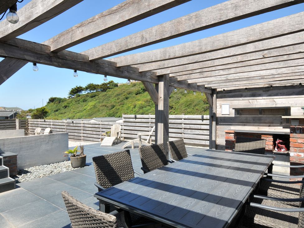 An outdoor dining area with a table and chairs under a pergola at Breakers View in Polzeath