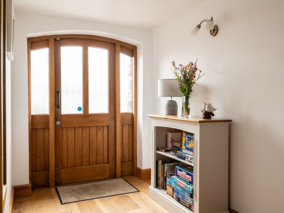 A hallway with a wooden door and a shelf displaying board games at Hoppers Barn Pancrasweek near Holsworthy