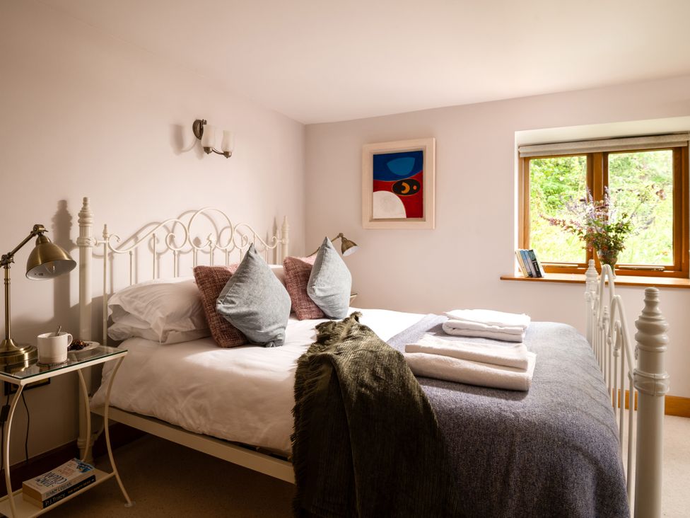 A bedroom with a bed, lamp, and window at Hoppers Barn Pancrasweek near Holsworthy