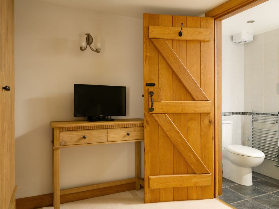 A bathroom with a television and wooden furniture at Hoppers Barn Pancrasweek near Holsworthy