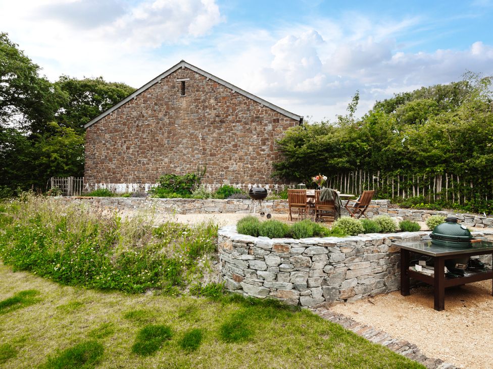 A garden with a dining area and stone features at Hoppers Barn Pancrasweek near Holsworthy