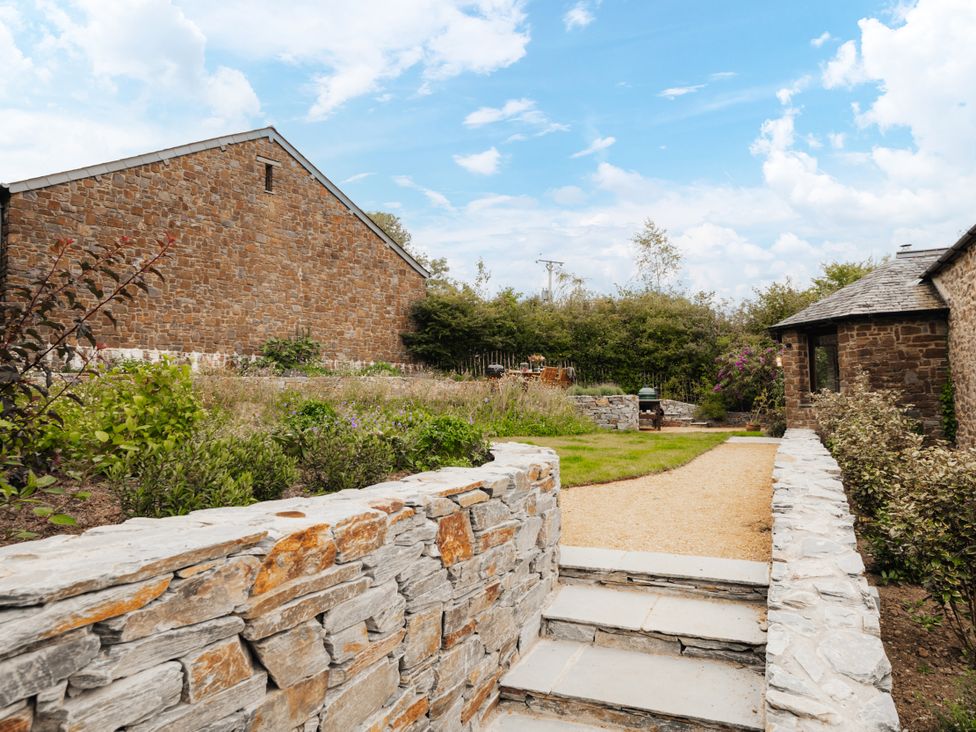 A garden with a stone wall and gravel path at Hoppers Barn Pancrasweek near Holsworthy