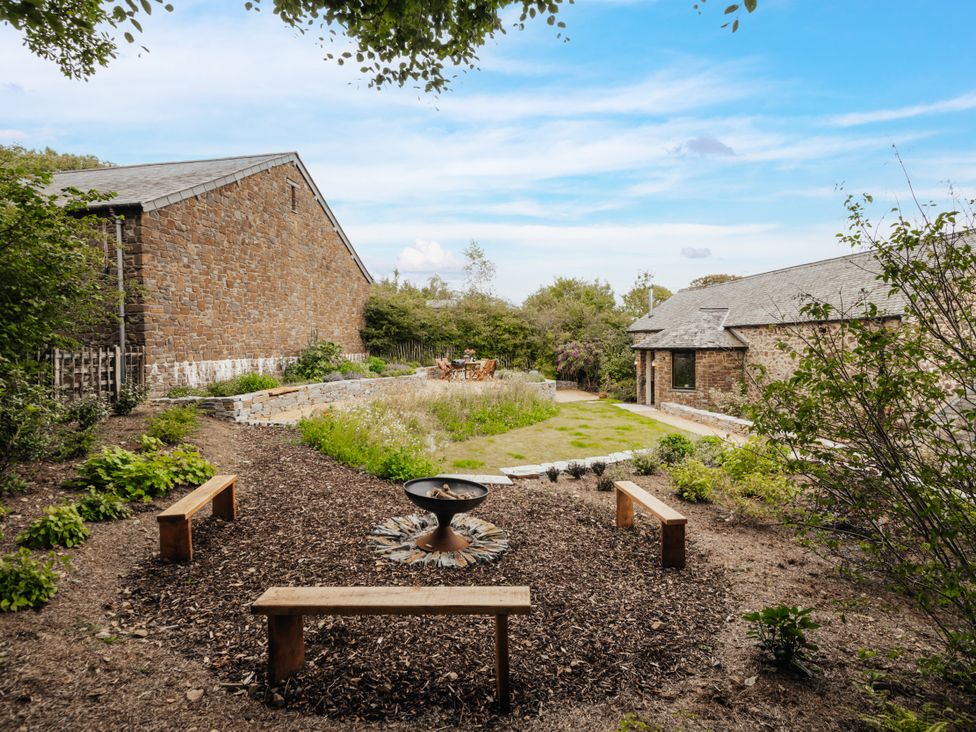 A garden with a fire pit and wooden benches at Hoppers Barn Pancrasweek near Holsworthy