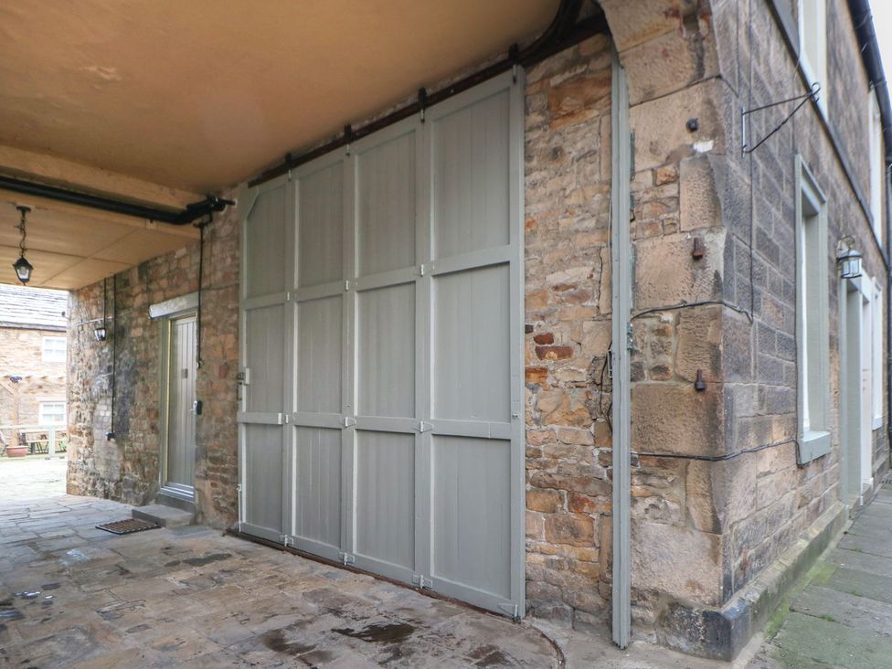 A garage with a stone wall and a gray garage door at The Smithy in Barnard Castle