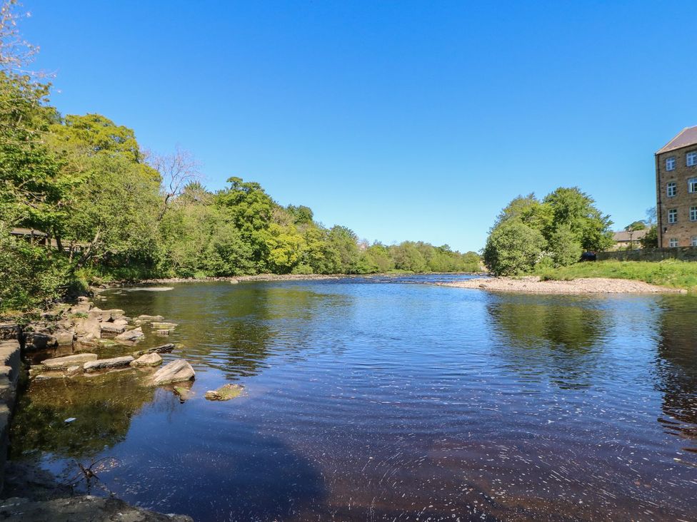 A river with trees and a building in the background at The Smithy in Barnard Castle