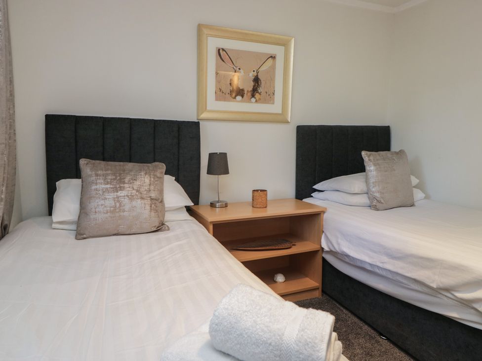 A bedroom with two beds and a bedside table at Treetops Beech Hill 13 ,Fallbarrow Park near Bowness-On-Windermere