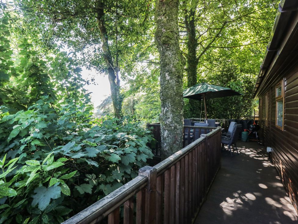 An outdoor area with a table and chairs under an umbrella at Treetops Beech Hill 13, Fallbarrow Park near Bowness-On-Windermere