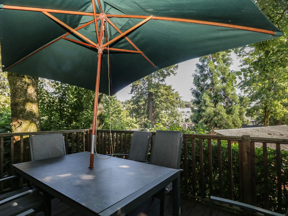 An outdoor seating area with a table and chairs under an umbrella at Treetops, Beech Hill 13, Fallbarrow Park near Bowness-On-Windermere