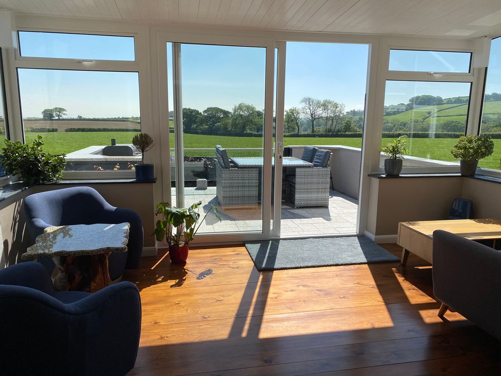 A sunlit living room with blue chairs plants and a wooden table overlooking a patio with outdoor furniture and green fields at Ashlea Launceston
