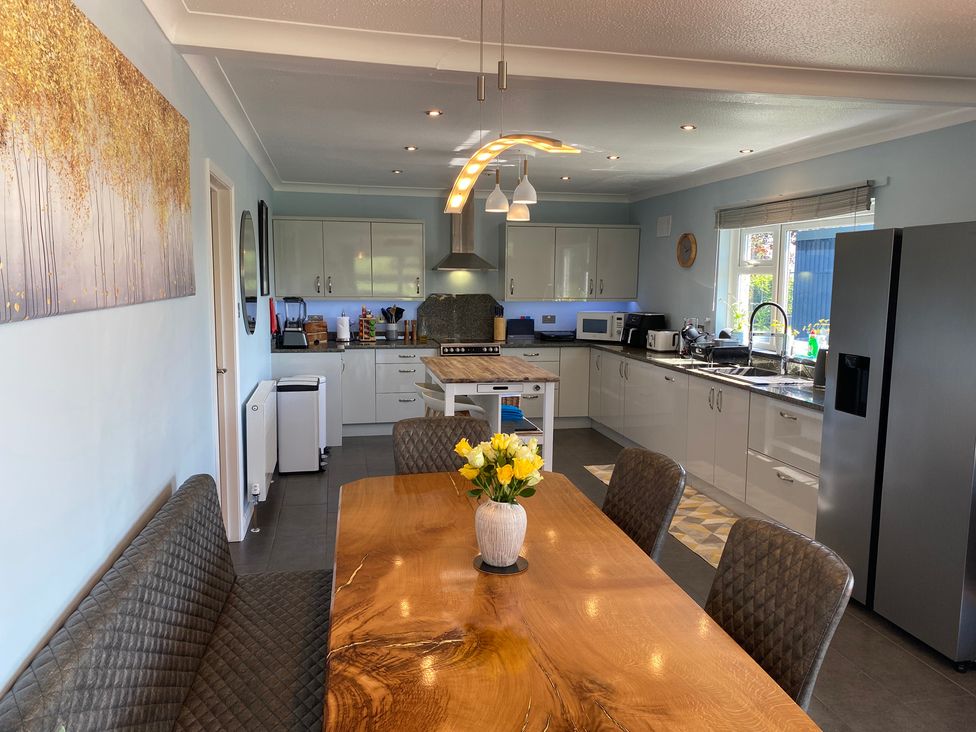 A kitchen with white cabinets a wooden dining table with chairs and a bench a vase with flowers a refrigerator and kitchen appliances at Ashlea in Launceston