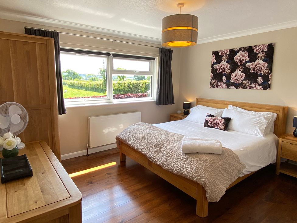 A bedroom with a wooden bed and side tables a window with dark curtains and a wooden dresser at Ashlea Launceston