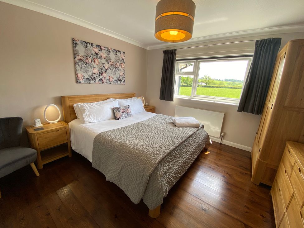 A bedroom with a double bed bedside tables a chair a wardrobe and a window showing a green field at Ashlea in Launceston
