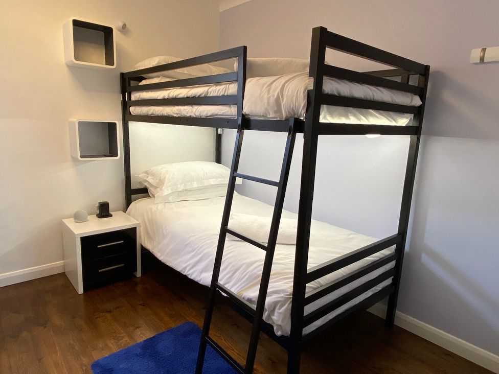 A bedroom with a black bunk bed white bedding a white nightstand and wall shelves at Ashlea in Launceston
