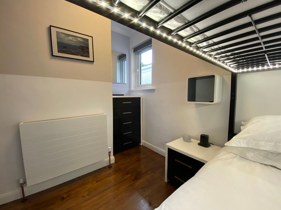A bedroom corner with a metal frame bunk bed above a white and black nightstand next to a window with a black chest of drawers and a wall-mounted shelf at Ashlea in Launceston