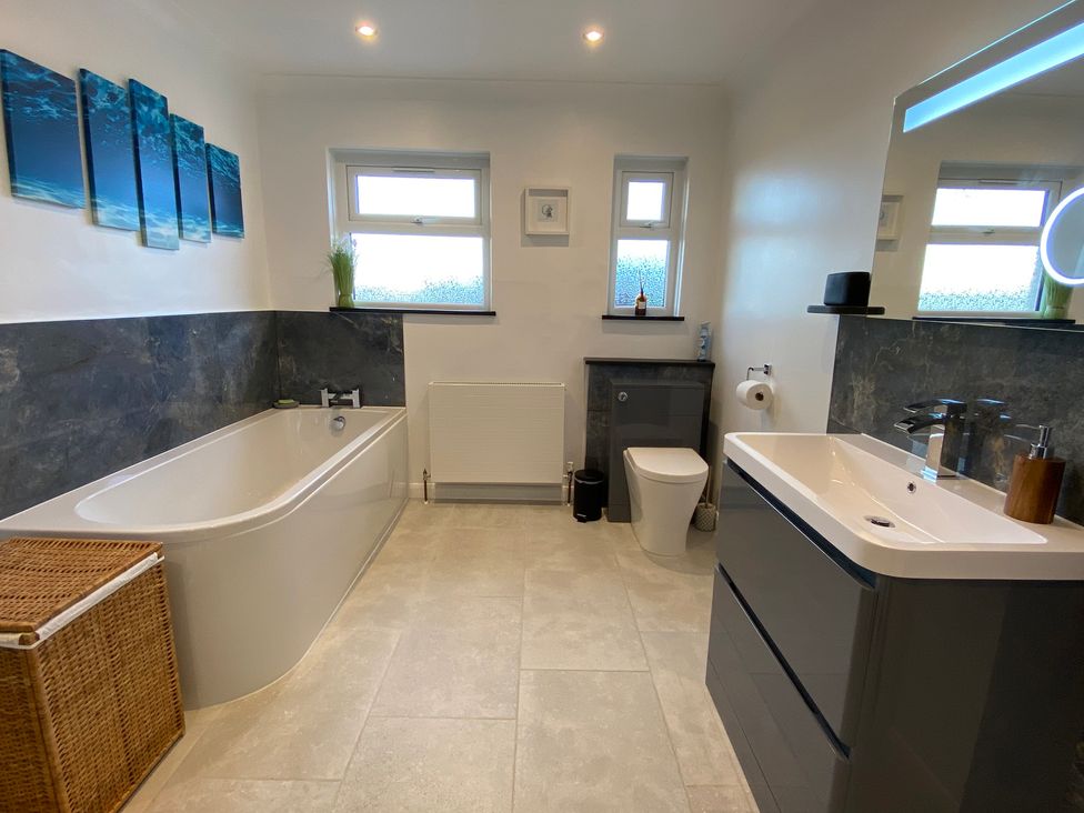 A bathroom with a bathtub a toilet a sink with a mirror and two windows at Ashlea in Launceston